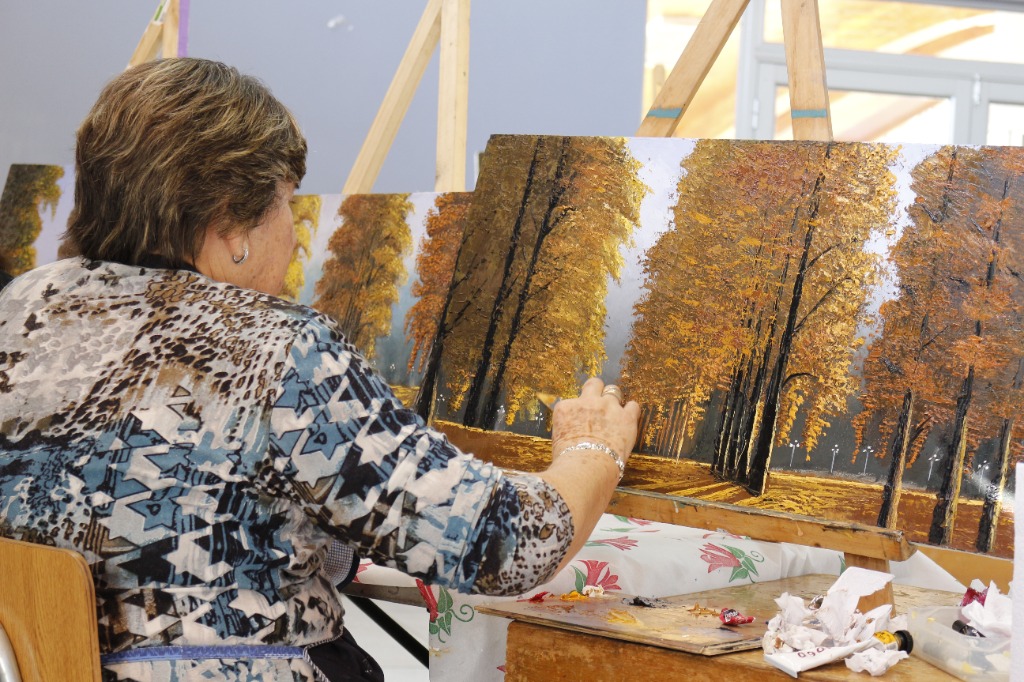 Alumna enfocada pintando paisaje otoñal de bosque en caballete